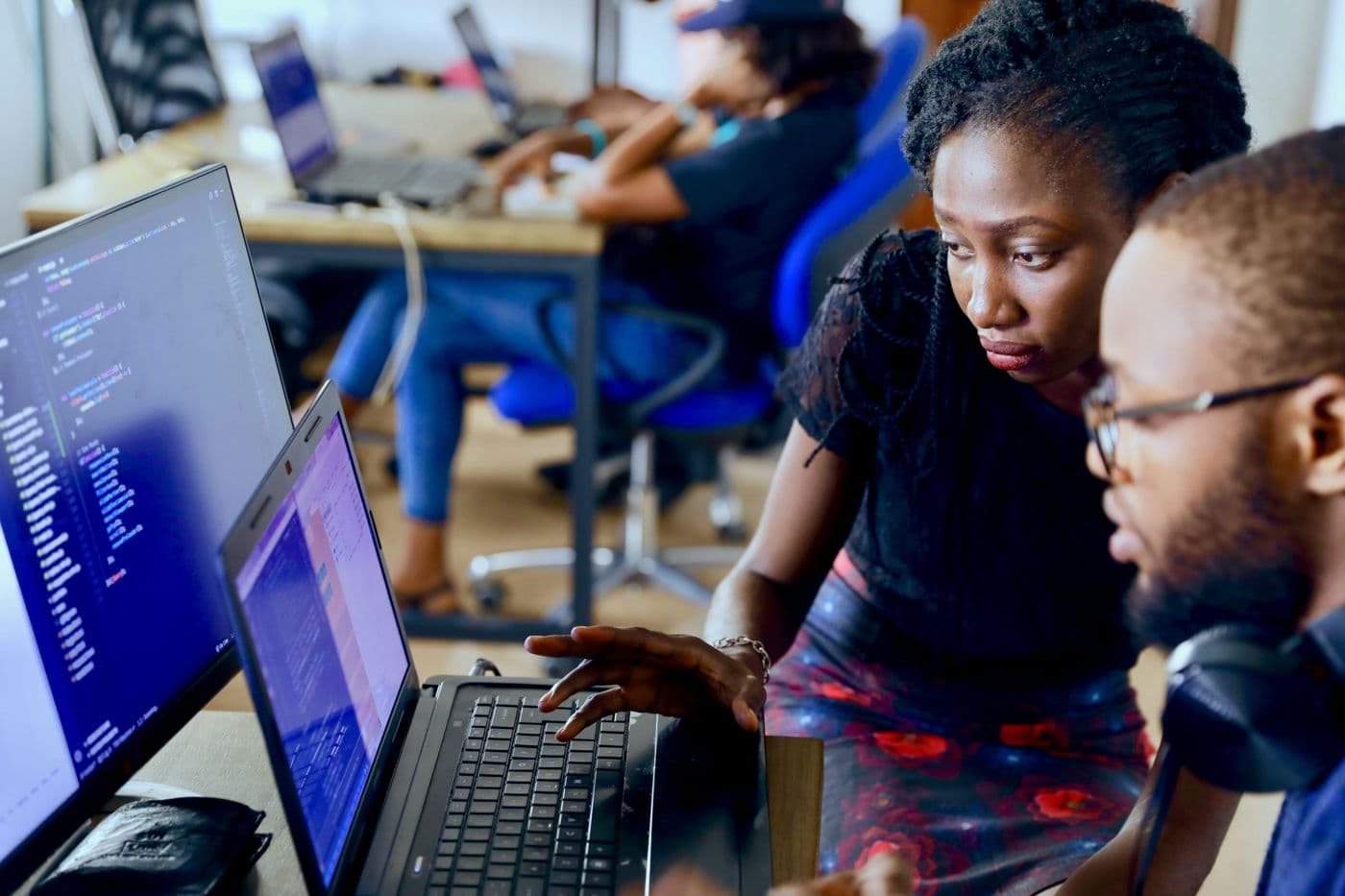 A coding teacher guiding an adult student at a laptop