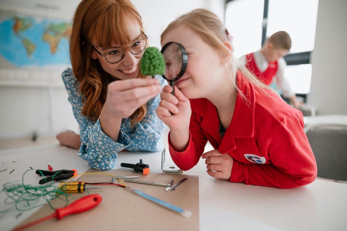 A teacher and a student exploring a model tree with a magnifying glass