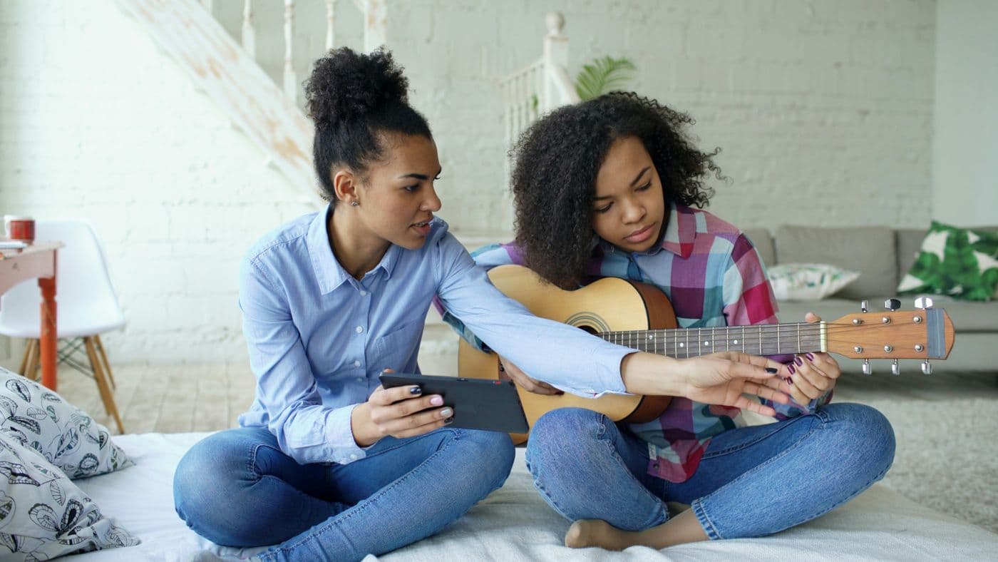 A guitar teacher showing a student a chord at home