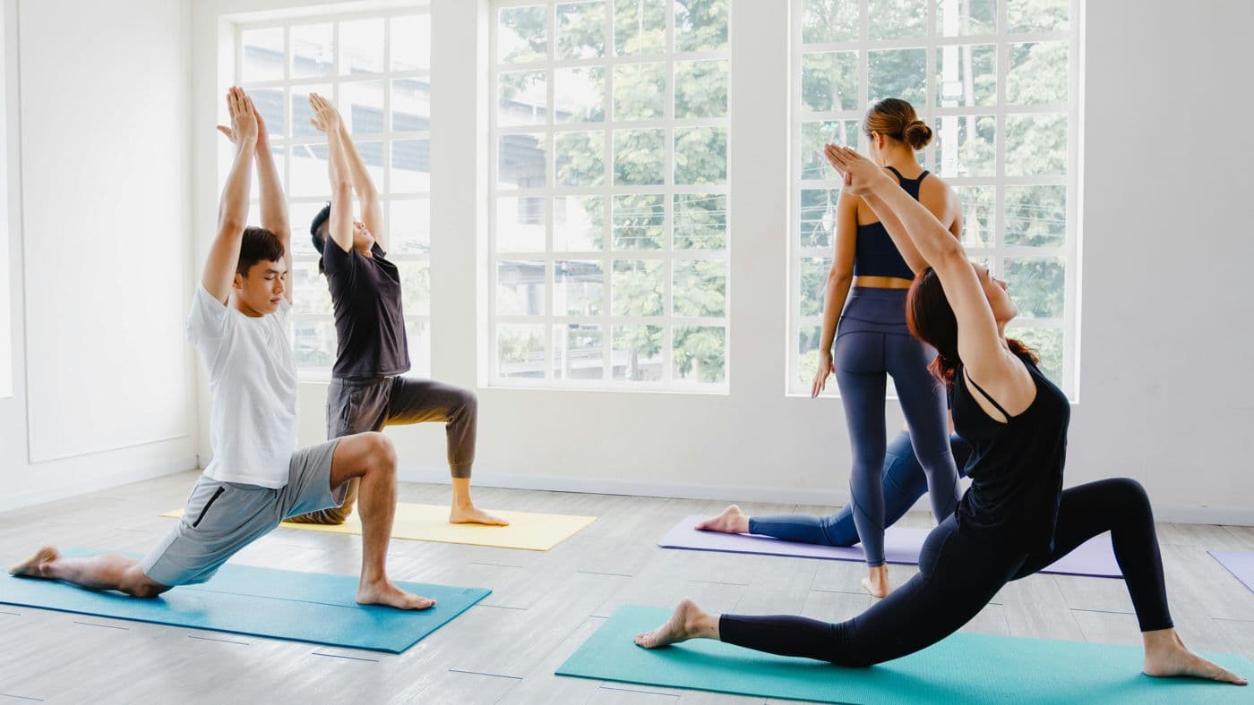 A yoga instructor walking between students in a bright studio